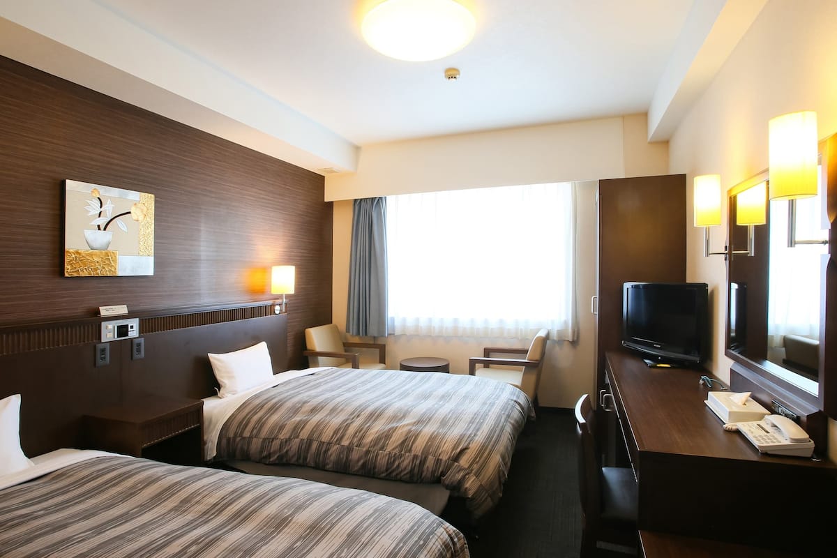 Ein Hotelzimmer mit zwei Betten, einem Schreibtisch mit Fernseher, einer Lampe und einem Gemälde an der Wand.