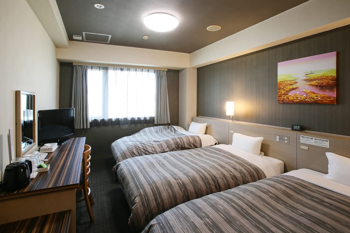 Ein Hotelzimmer mit zwei Betten, einem Schreibtisch mit Fernseher, einem Bild an der Wand und einem Fenster mit Vorhängen.