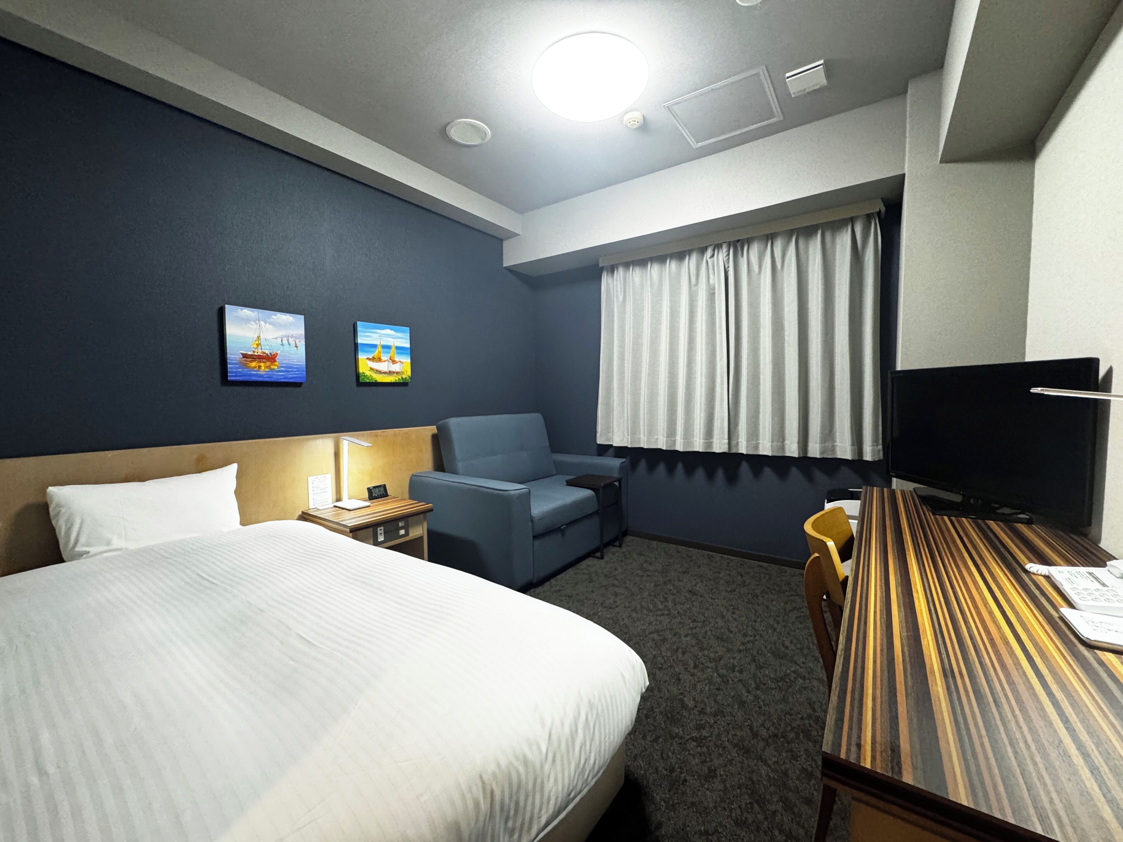 Ein Hotelzimmer mit einem Bett, einem Schreibtisch, einem Stuhl, einem Fernseher und zwei Bildern an der Wand.
