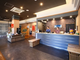 Una moderna zona de recepción de hotel con un mostrador, dos empleados, un peluche y una planta pequeña.