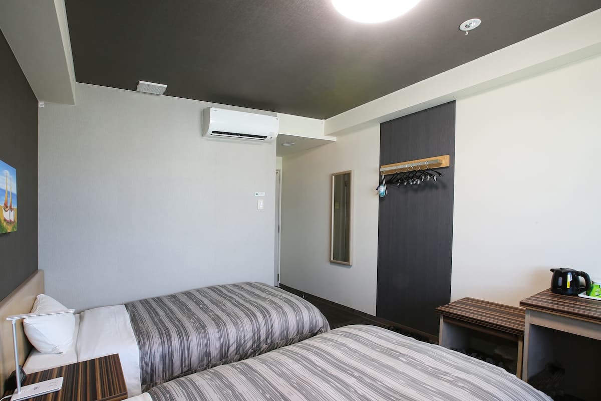 Ein Hotelzimmer mit zwei Betten, einem Schreibtisch mit Wasserkocher und einer Wandklimaanlage.