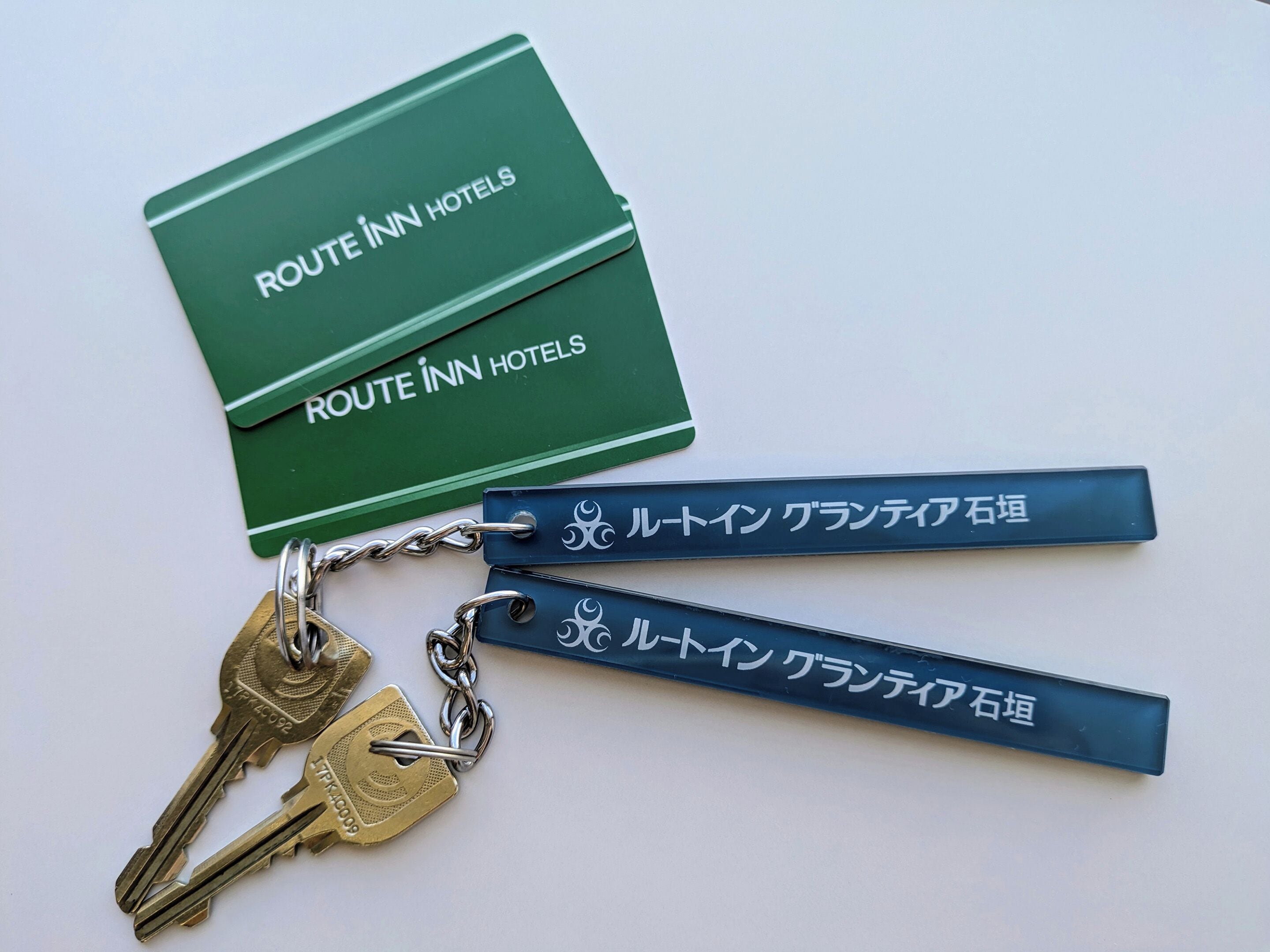 Una tarjeta verde y dos llaveros con texto japonés, probablemente para un hotel llamado Route Inn Hotels.
