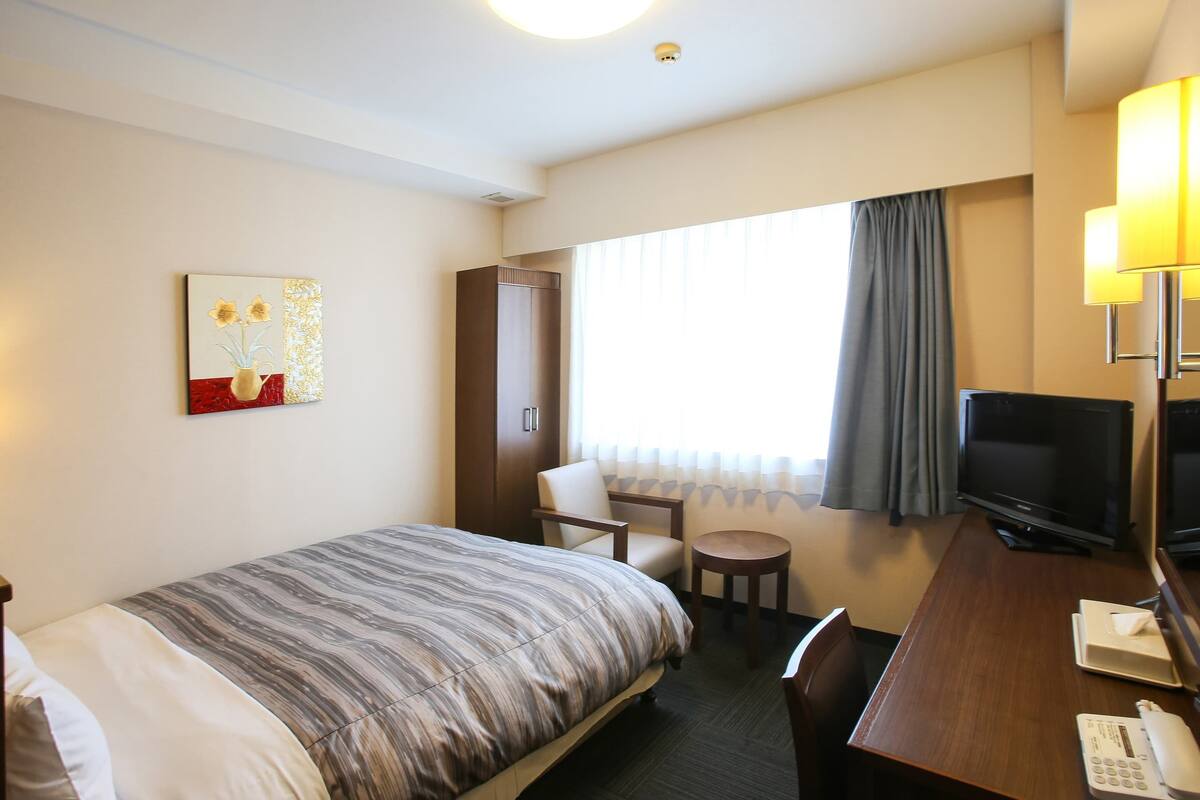 Ein Hotelzimmer mit Bett, Schreibtisch, Stuhl, Fernseher und Telefon.