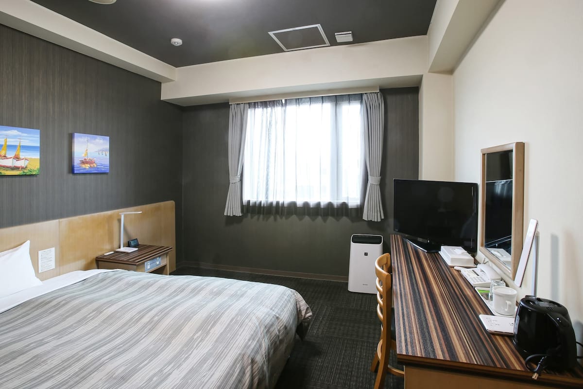 Ein Hotelzimmer mit Bett, Schreibtisch, Stuhl, Fernseher und einem Fenster mit Vorhängen.