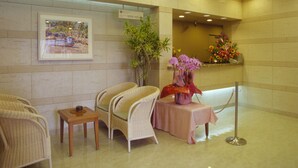 Zona de recepció amb cadires de vimet, una taula petita, un quadre amb marc, una planta en test i un arranjament floral.