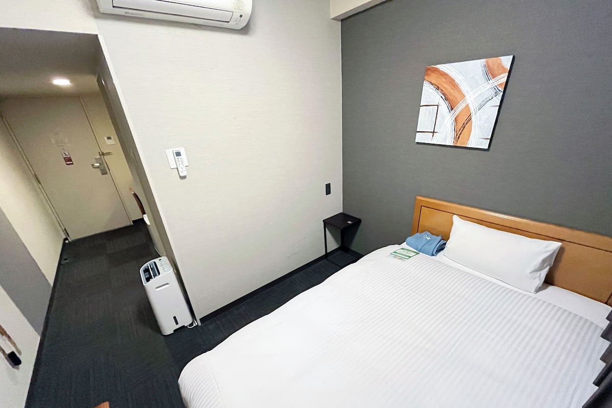 Une chambre d’hôtel avec un lit, une table de chevet, un climatiseur fixé au mur et un tableau.