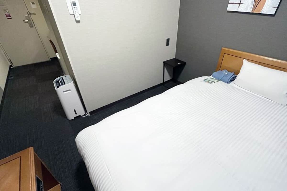Une chambre d’hôtel comprenant un lit, une petite table de chevet, une poubelle et un panneau de commande fixé au mur.