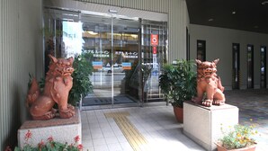 Entrada d'un edifici amb una porta de vidre, dues estàtues de lleó i plantes en testos.