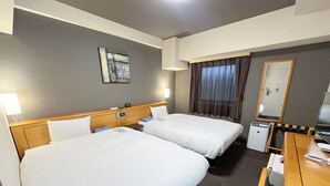 Habitació d'hotel amb dos llits, un escriptori, una cadira, una làmpada, un mirall i una finestra amb cortines.