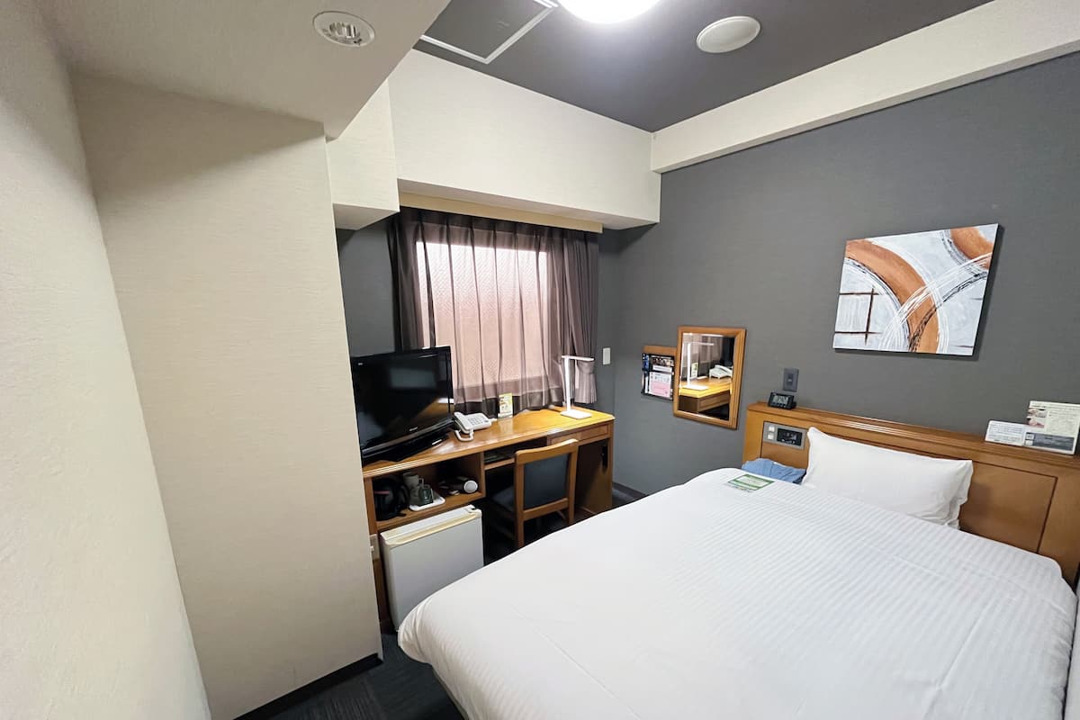 Une chambre d’hôtel avec un lit, un bureau avec une télévision, un petit réfrigérateur, un téléphone et un tableau au mur.