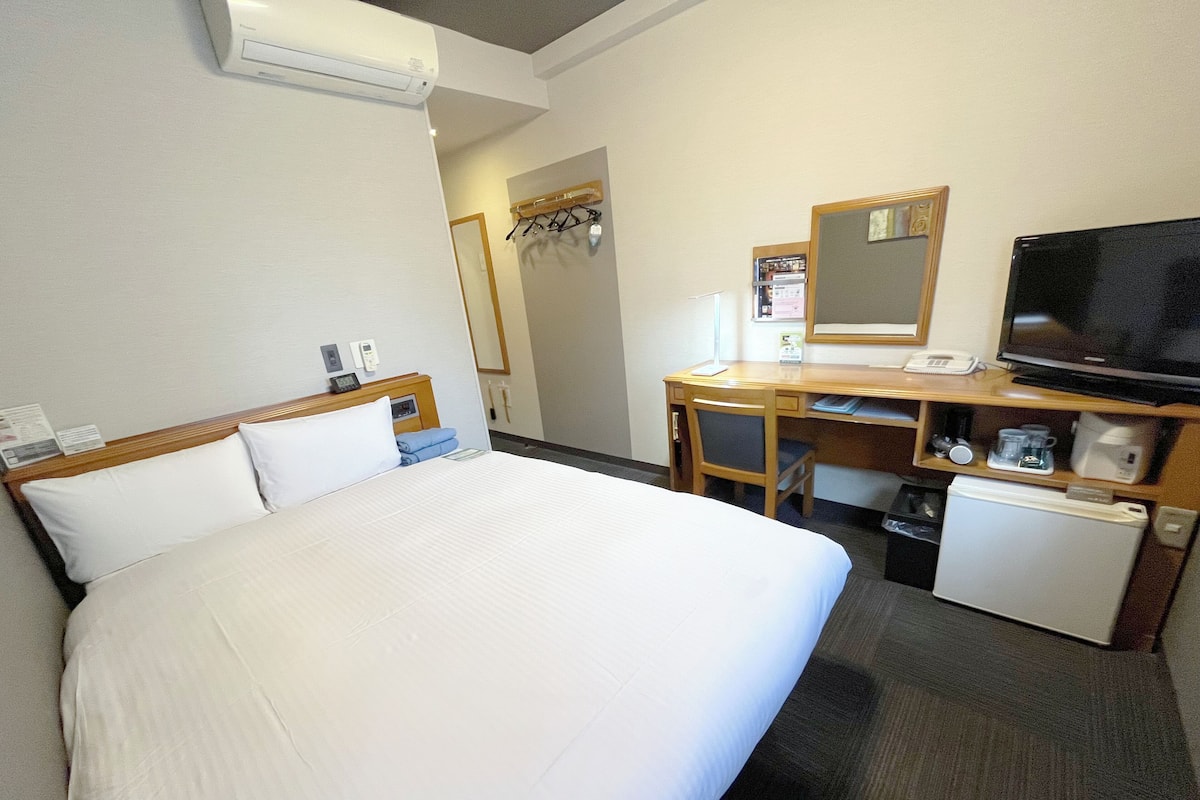 Une chambre d’hôtel équipée d’un lit, d’un bureau avec un ordinateur, d’une télévision, d’un mini-réfrigérateur et d’un petit réfrigérateur.