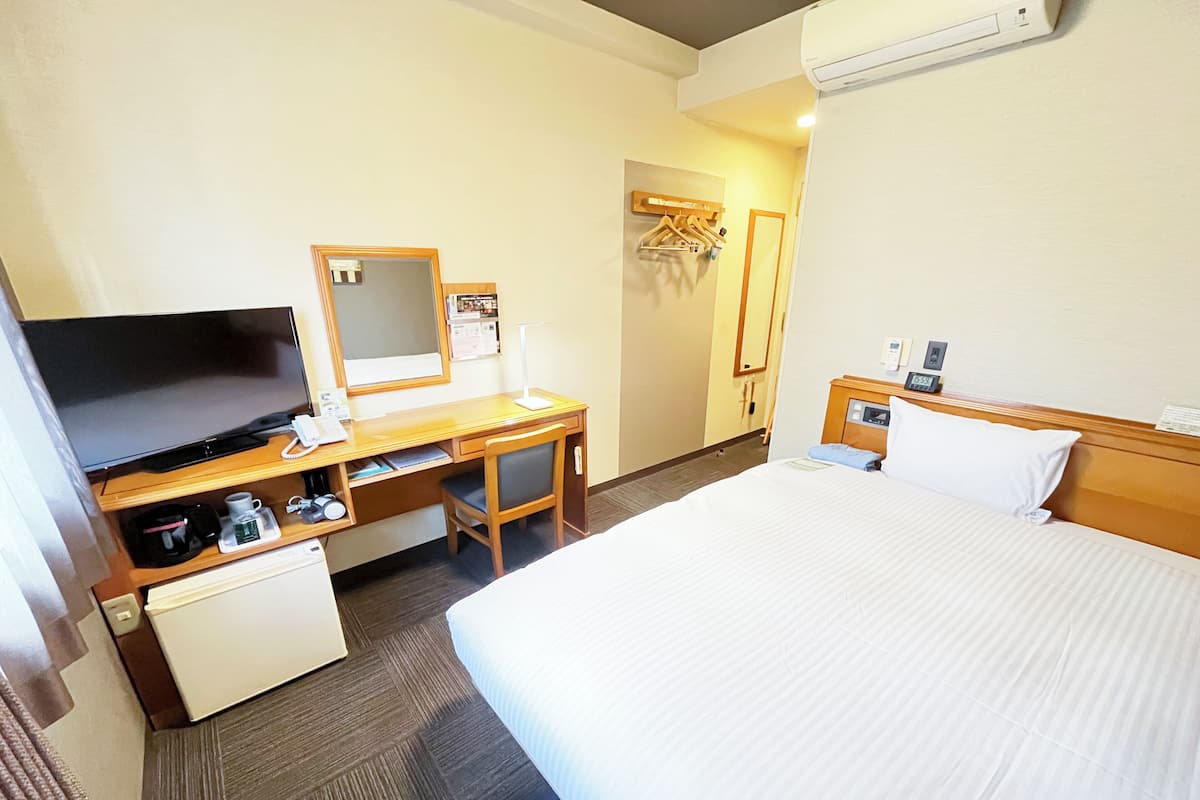 Une chambre d’hôtel équipée d’un lit, d’un bureau, d’une télévision et d’un petit réfrigérateur.