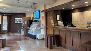 A reception area with a wooden counter, a digital screen, a menu stand, and a small seating area. - Hotel Route-Inn Dai-Ichi Nagano (Nagano)