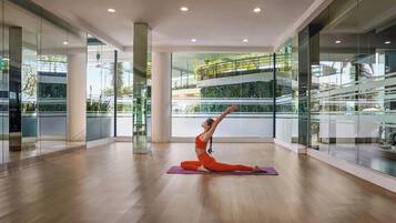 A spacious indoor area with glass walls, a wooden floor, and a person performing a yoga pose on a purple mat.