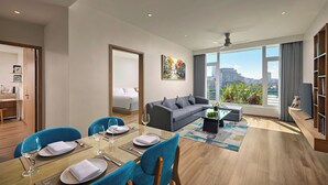 Un soggiorno moderno con zona pranzo, un divano grigio, una TV e una grande finestra vista città.