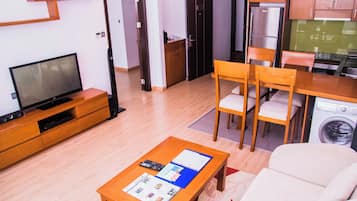 A modern living room with a flat-screen TV, wooden furniture, a dining area with chairs, and a washing machine.
