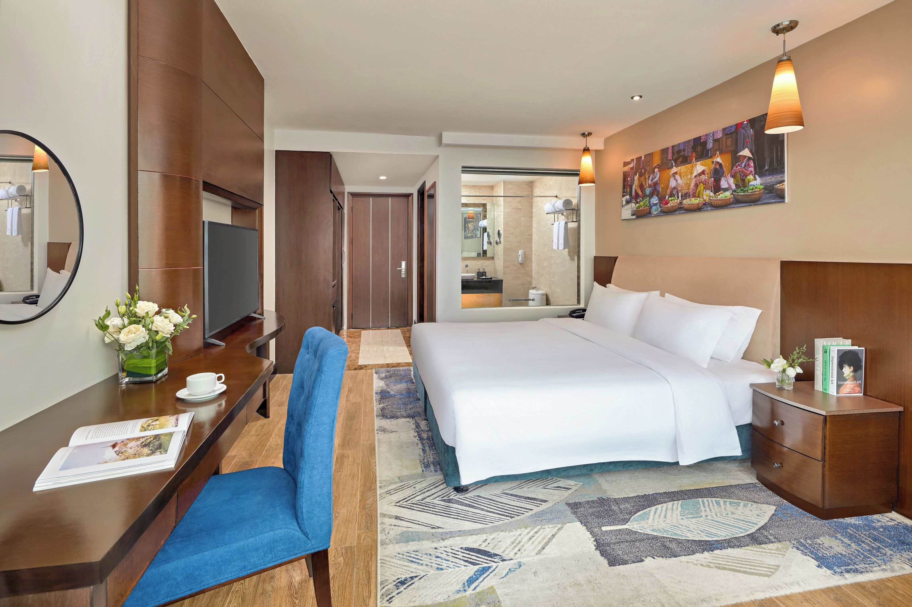 Habitación de hotel con una cama grande, un escritorio con silla, una mesita de noche, un espejo y un cuadro en la pared.