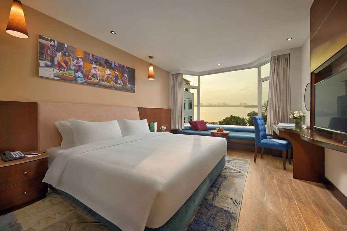 A hotel room with a large bed, a desk with a TV, a sofa, and a view of a body of water.