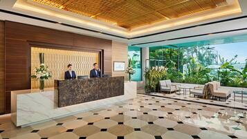 A modern hotel lobby with a reception desk, seating area, and large windows overlooking greenery.