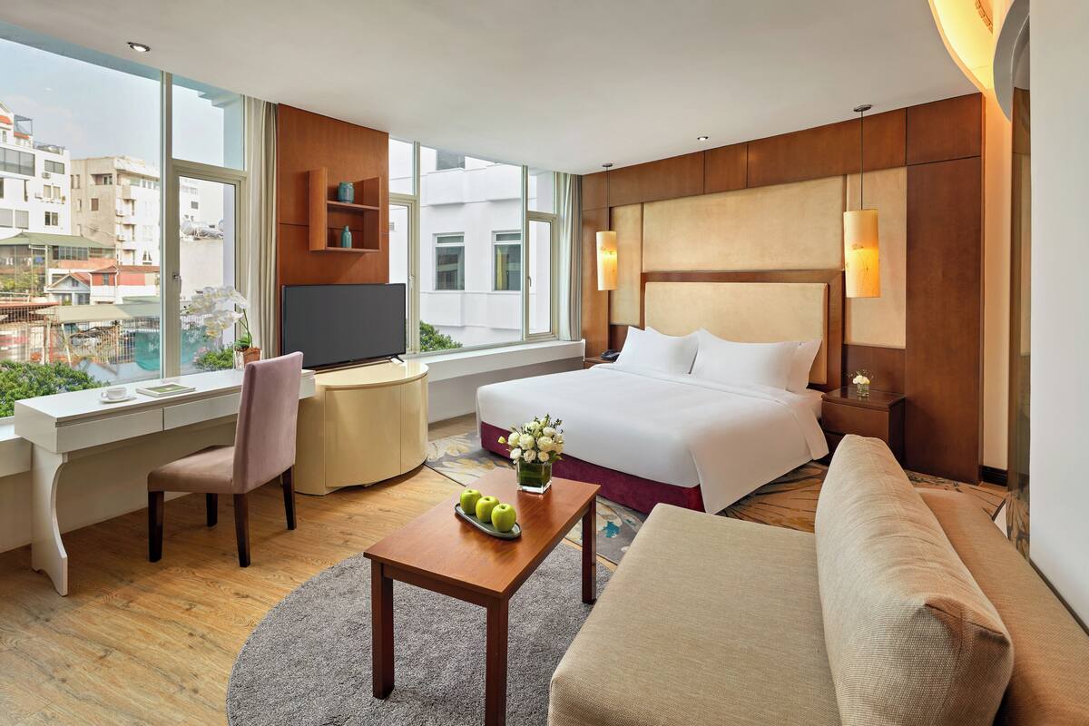 A hotel room with a bed, a desk, a chair, a sofa, and a TV.