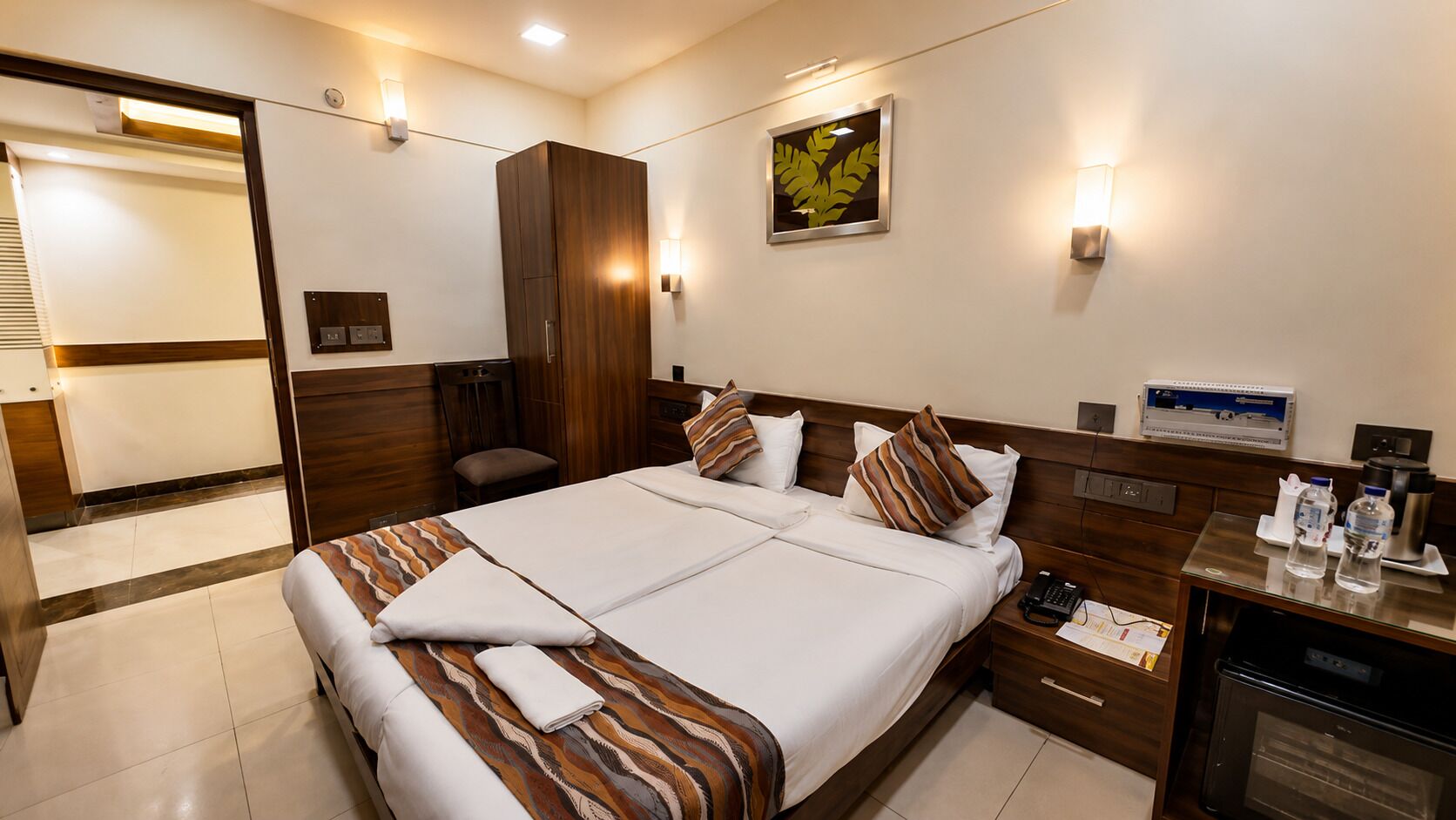 A hotel room with a bed, bedside tables, a desk, a chair, and a wardrobe.