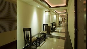 Ein Hotelkorridor mit einer Sitzecke, die einen Glastisch und Stühle, einen Fliesenboden und eingelassene Beleuchtung umfasst.
