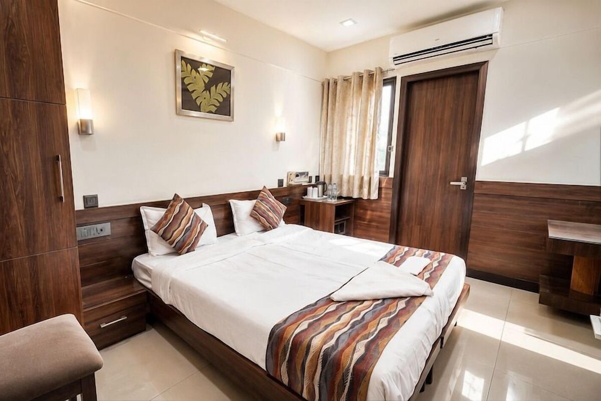 A hotel room with a large bed, wooden wardrobe, bedside table, and a wall-mounted air conditioner.