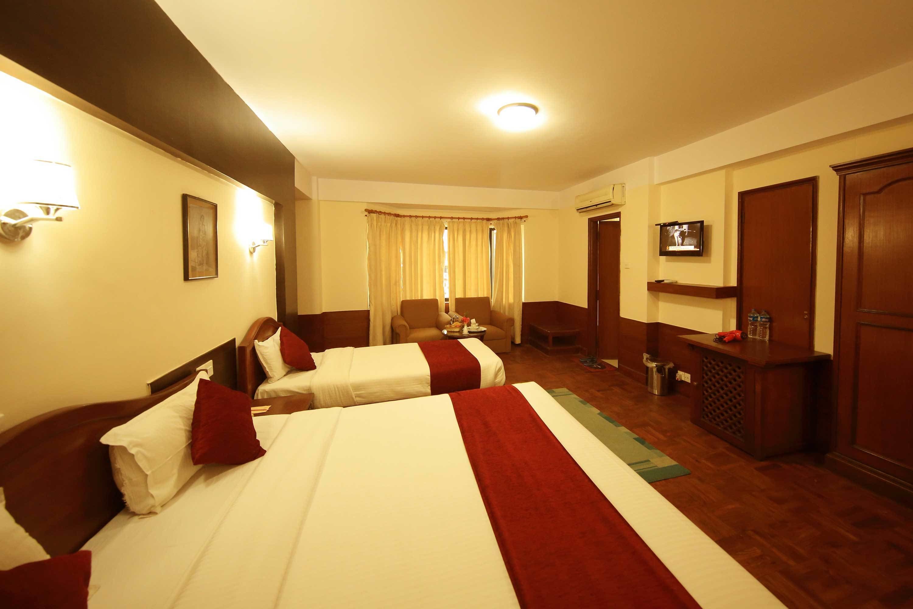 A hotel room with two beds, a television, a desk, and a window with curtains.