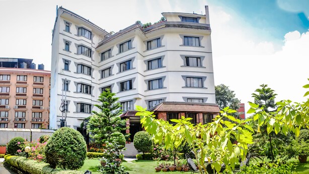 Un hôtel à plusieurs étages doté d’une cour intérieure, entourée d’une végétation luxuriante et d’un jardin bien entretenu.
