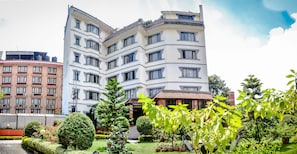 A multi-story hotel with a central courtyard, surrounded by lush greenery and a well-maintained garden.