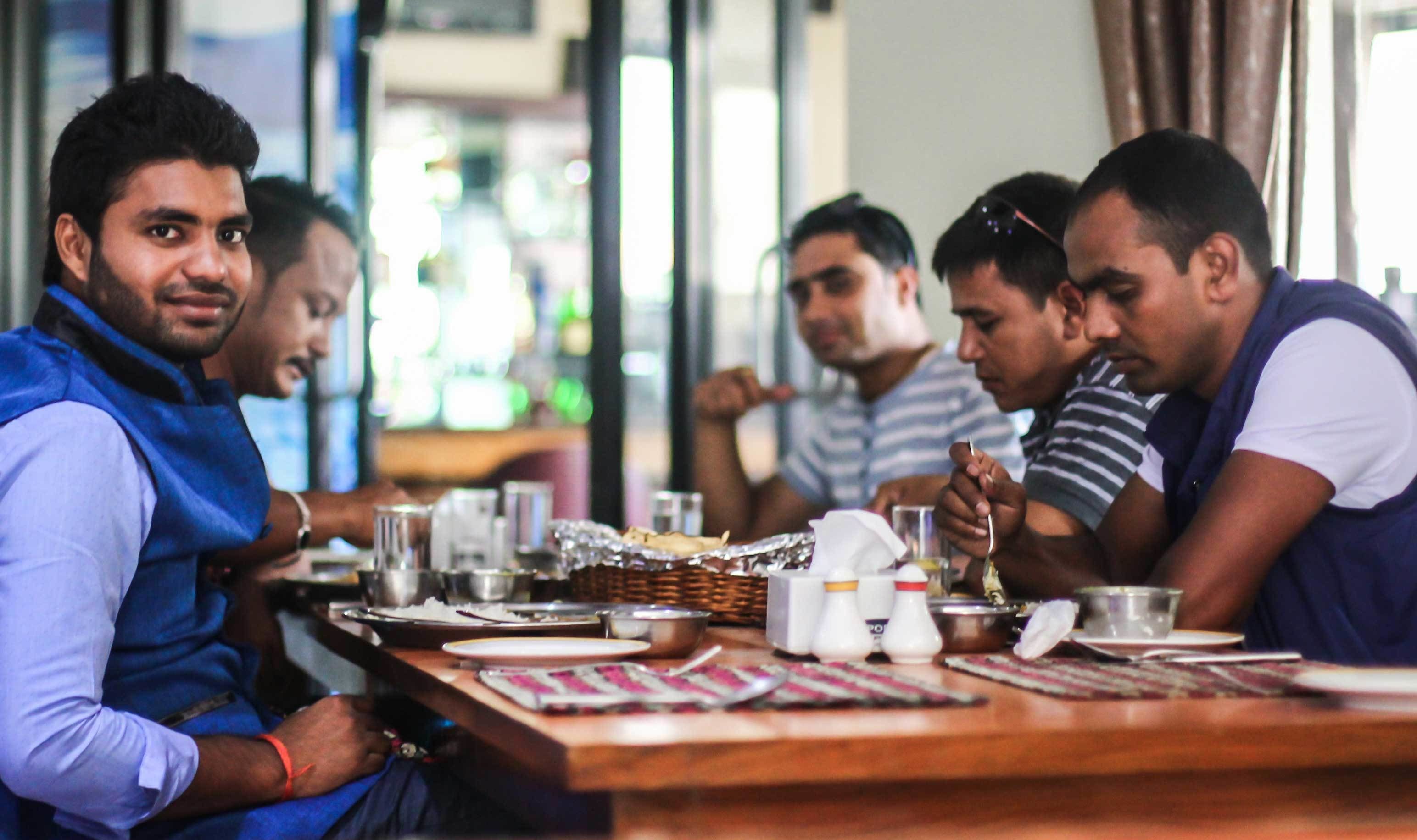 A group of people dining at a restaurant with a wooden table, various dishes, and condiments.