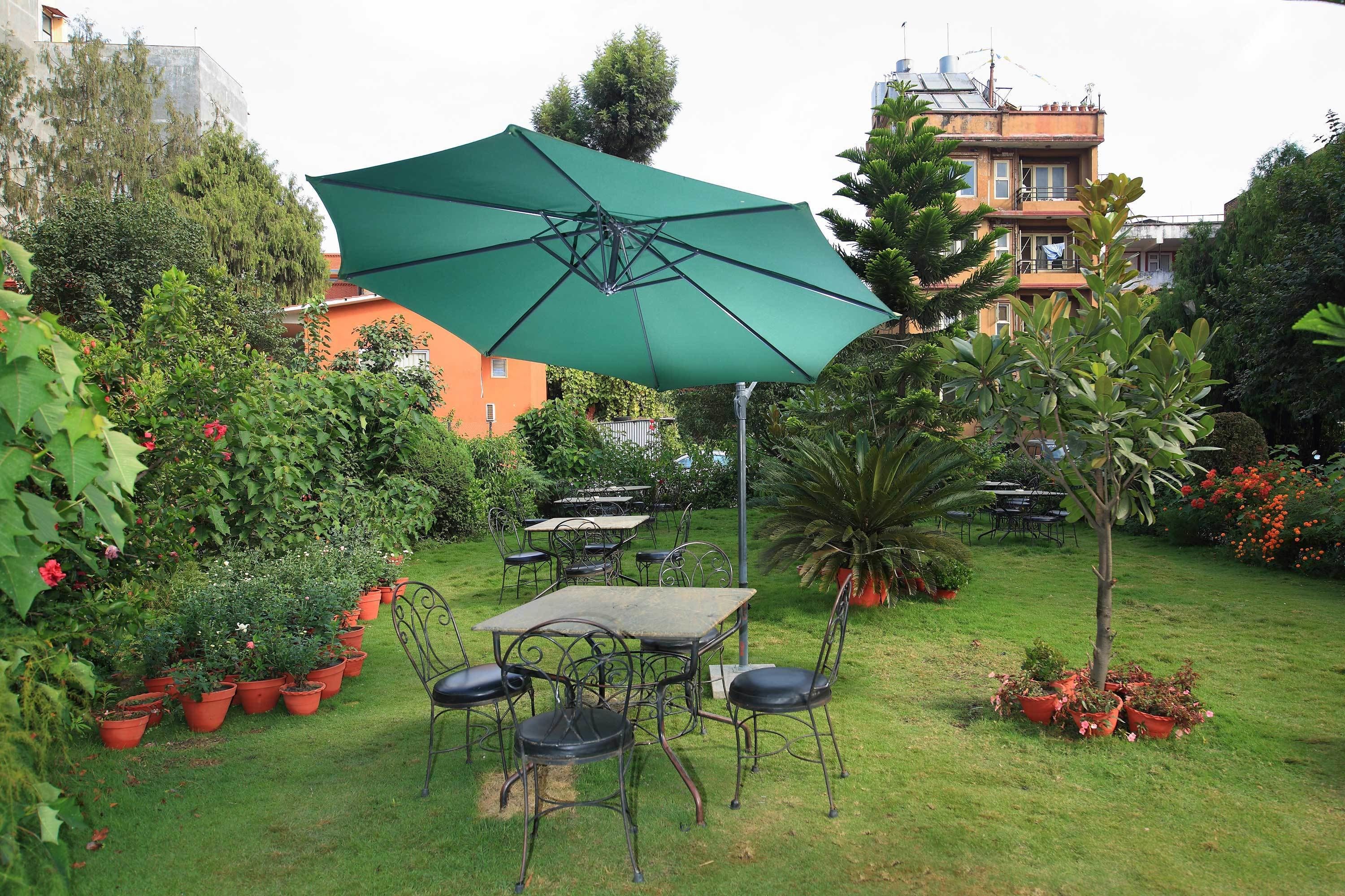 An outdoor patio with a table and chairs, surrounded by potted plants and a green umbrella.