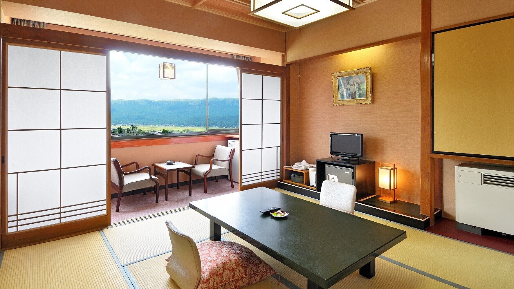 Ein traditioneller japanischer Raum mit Tatami-Bodenbelag, einem niedrigen Tisch, einer Couch, einem Fernseher und Blick auf die Berge.