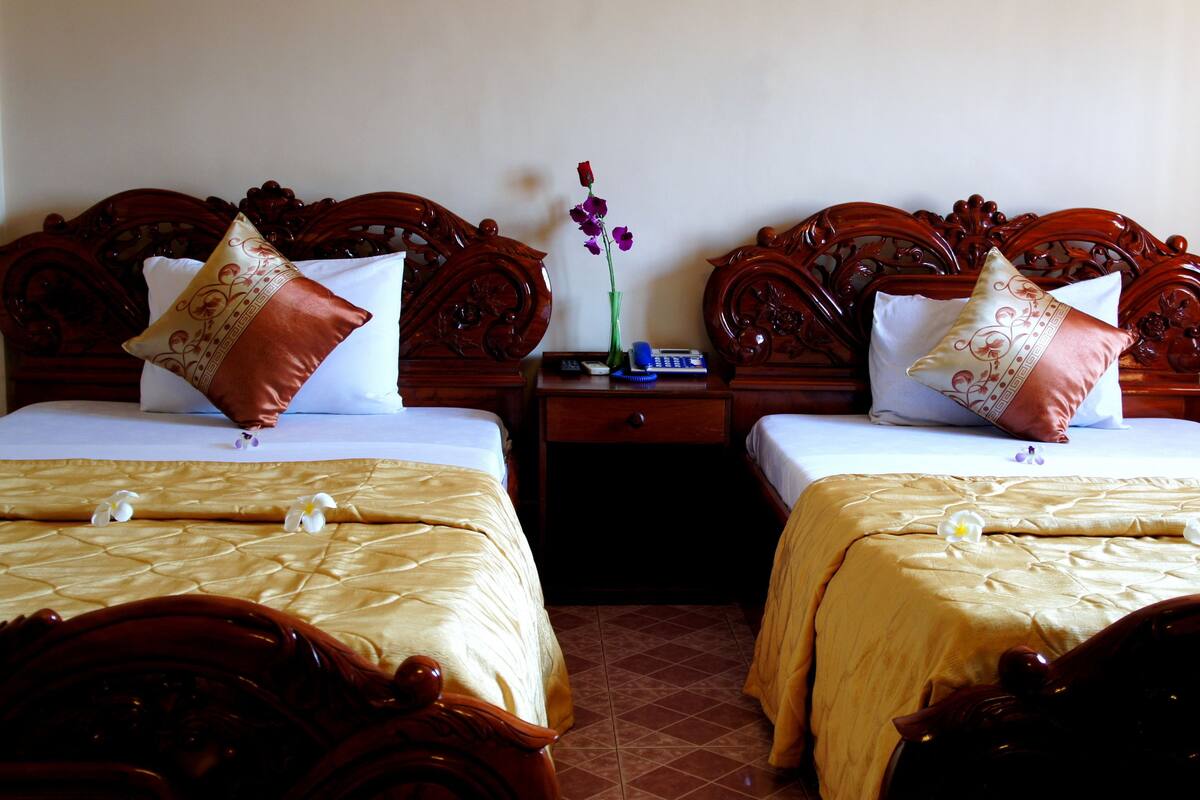 Two double beds with wooden headboards, a nightstand with a phone and vase, and a tiled floor.
