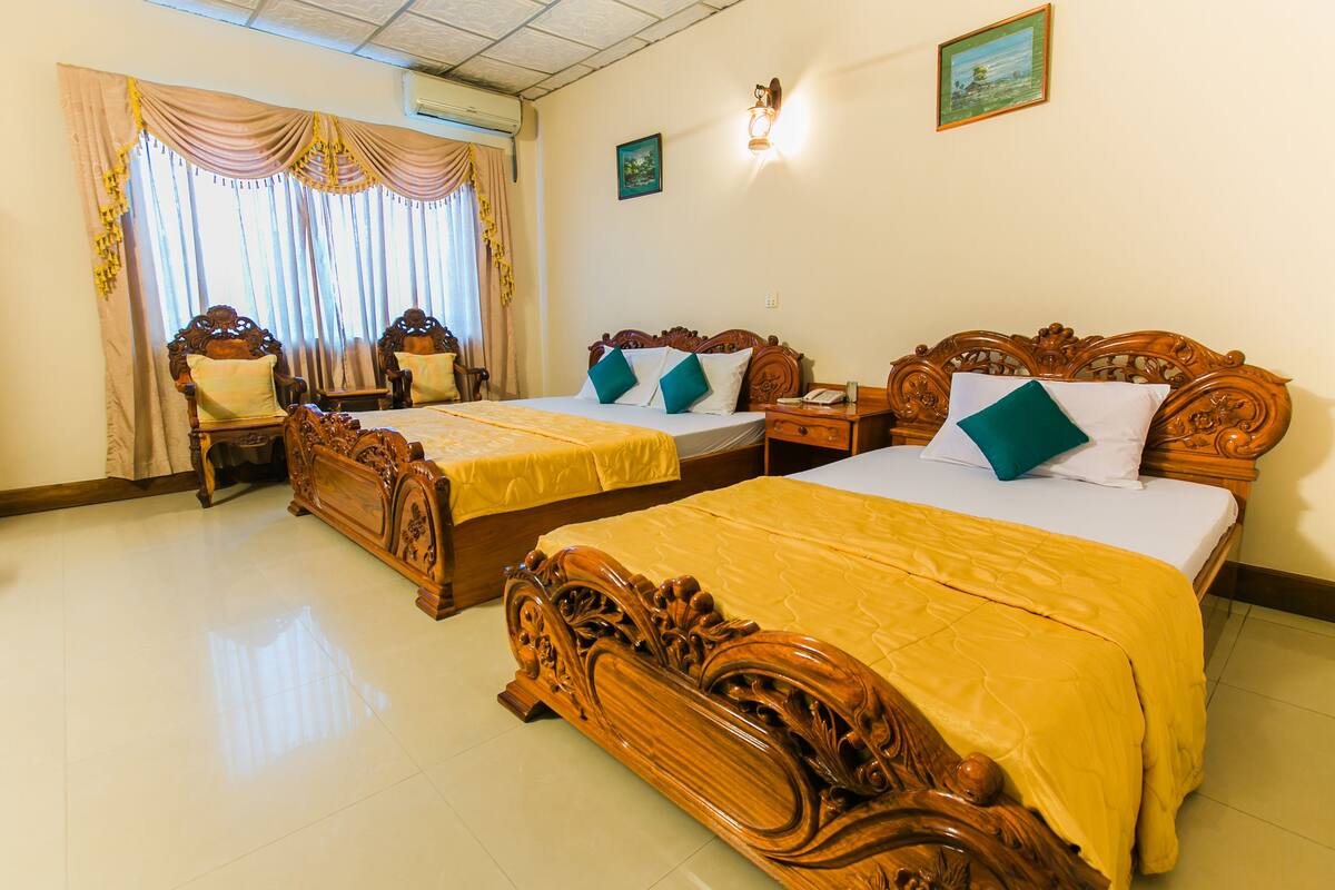 A hotel room with two wooden beds, a nightstand, a chair, and a large window with curtains.