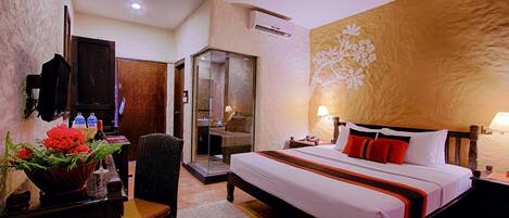 A hotel room with a large bed, a desk with a chair, a TV, and a wall-mounted air conditioner.