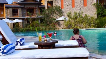 Zona junto a la piscina con sillones, sombrillas y una mesa con bebidas.