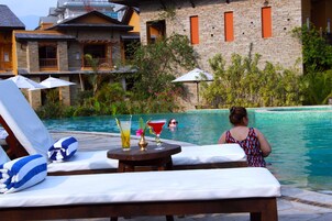 Zona junto a la piscina con sillones, sombrillas y una mesa con bebidas.