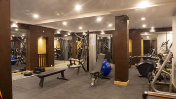 Un gimnasio con equipos de ejercicio variados, espejos y una banca.