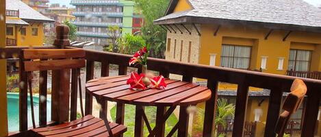 Un balcón de madera con mesa y sillas, con vistas a una piscina y edificios coloridos.