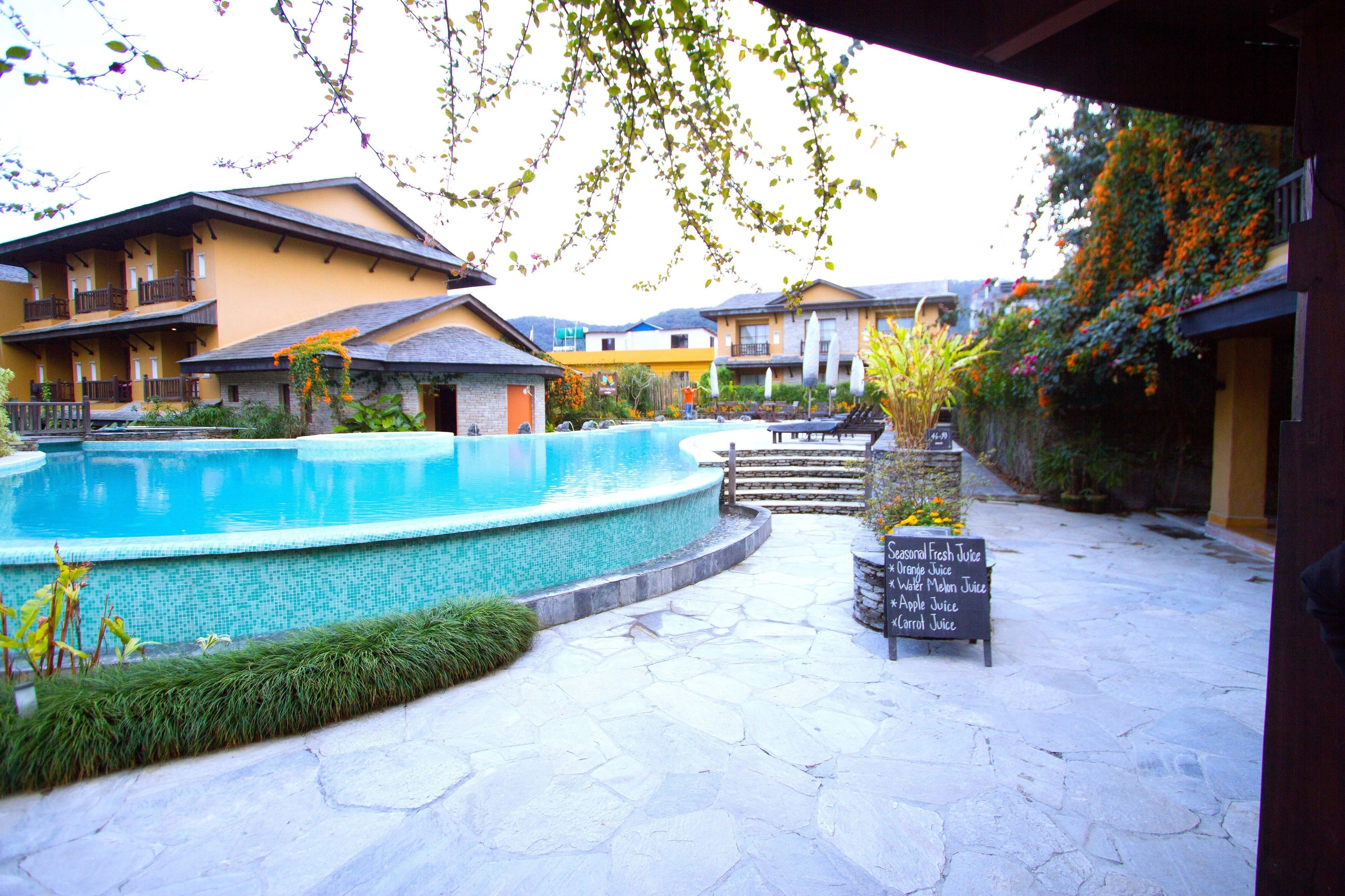A courtyard with a swimming pool, stone flooring, and a sign listing juice options.
