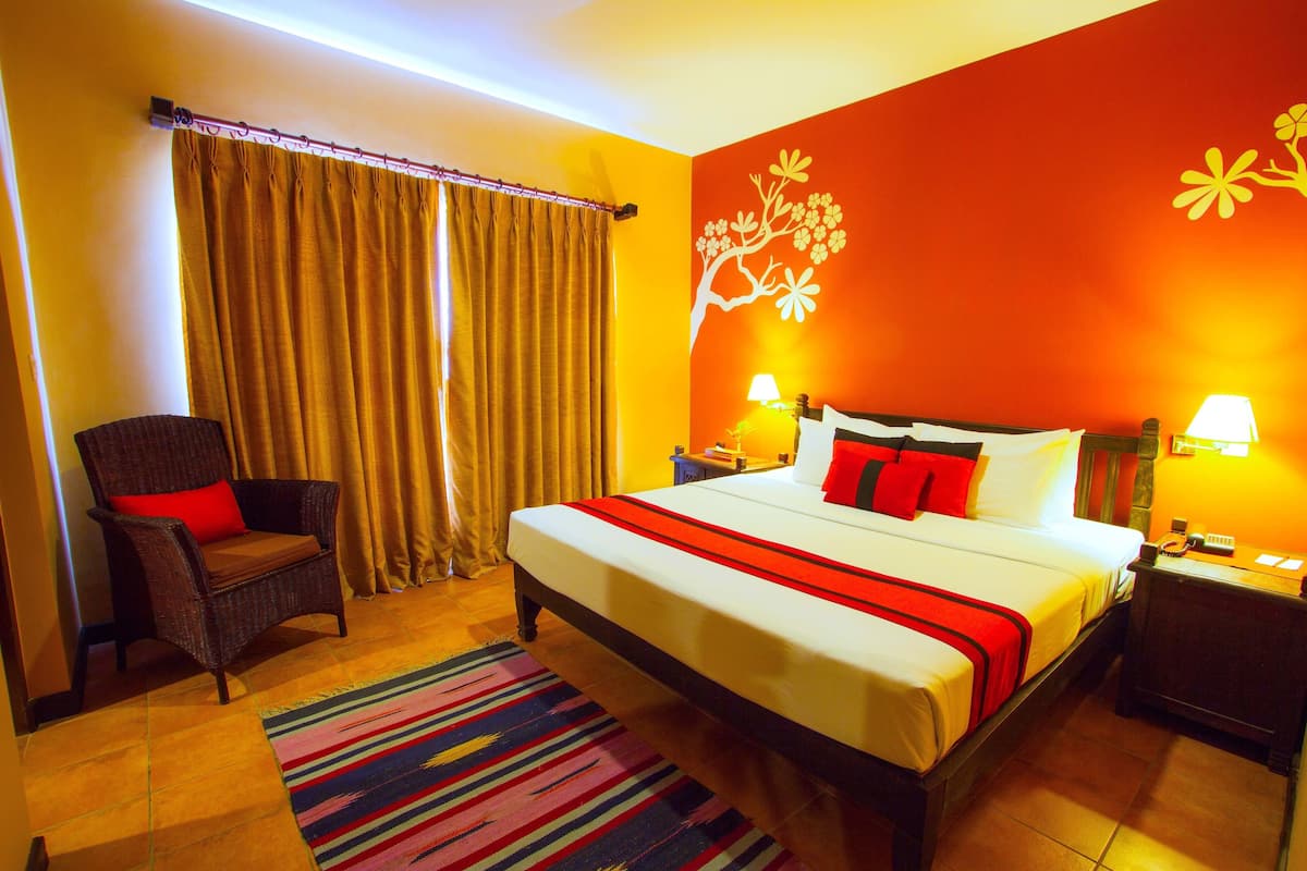 A hotel room with a large bed, a chair, a nightstand, and a wall with a tree design.