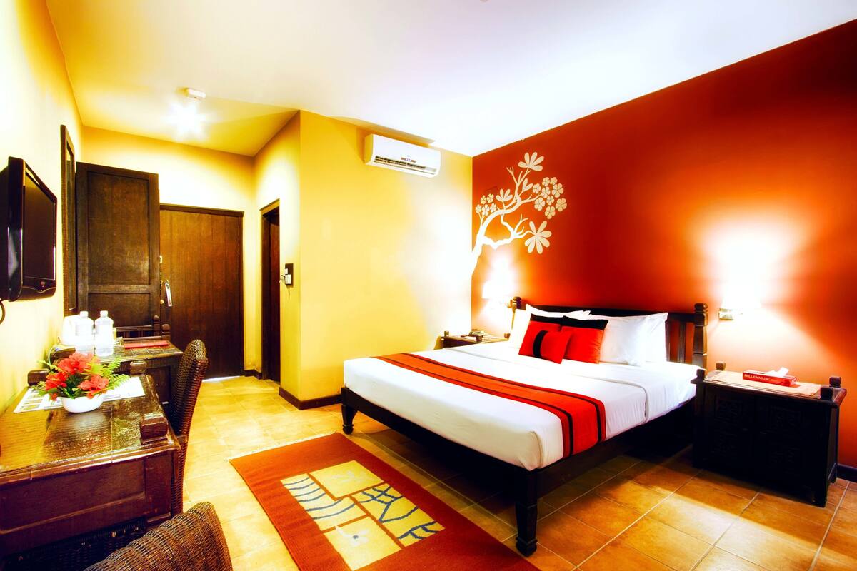 A hotel room with a bed, a desk, a chair, a TV, and a wall-mounted air conditioner.