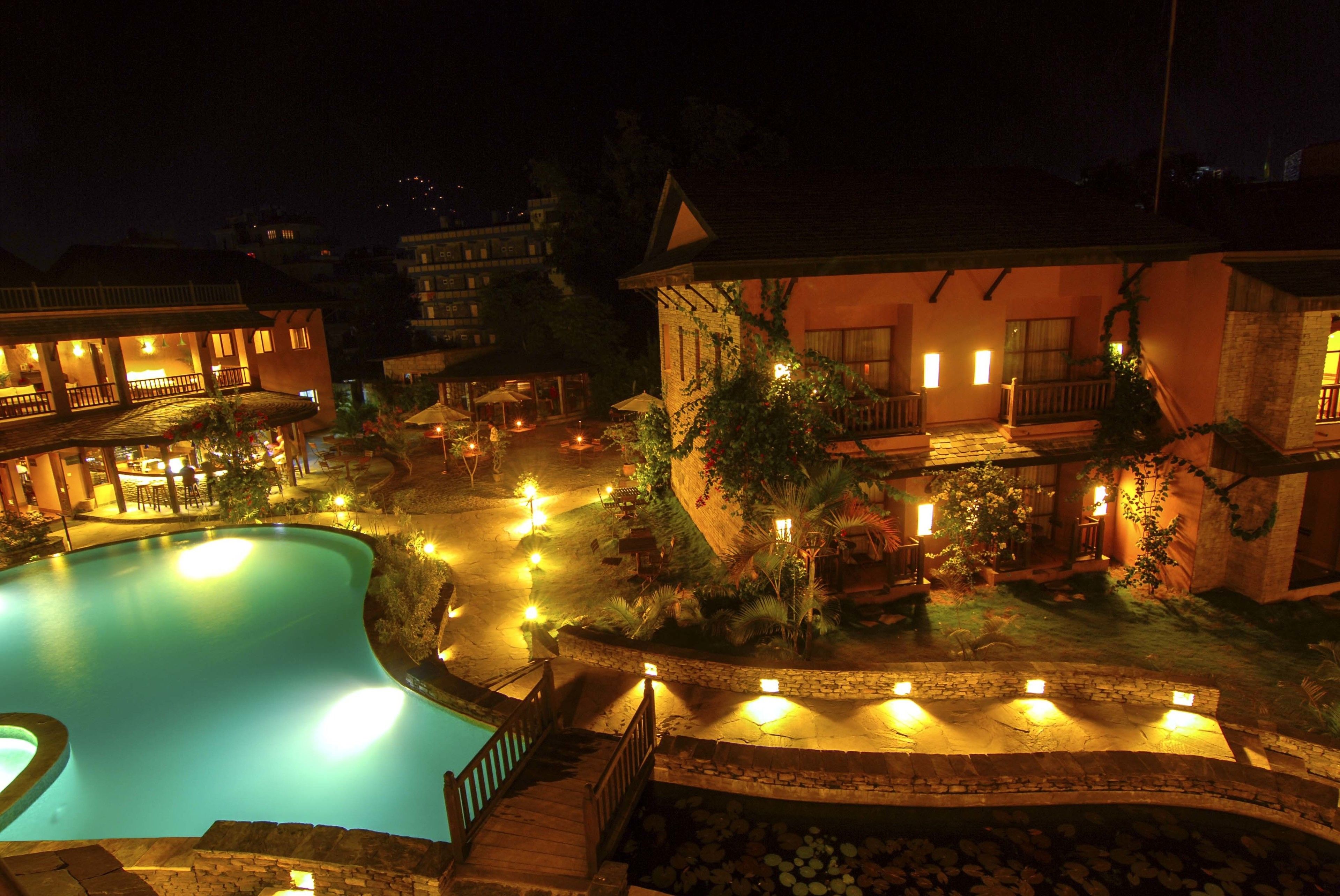Vue nocturne d’un complexe hôtelier doté d’une piscine, d’espaces de détente en plein air et de chemins éclairés.