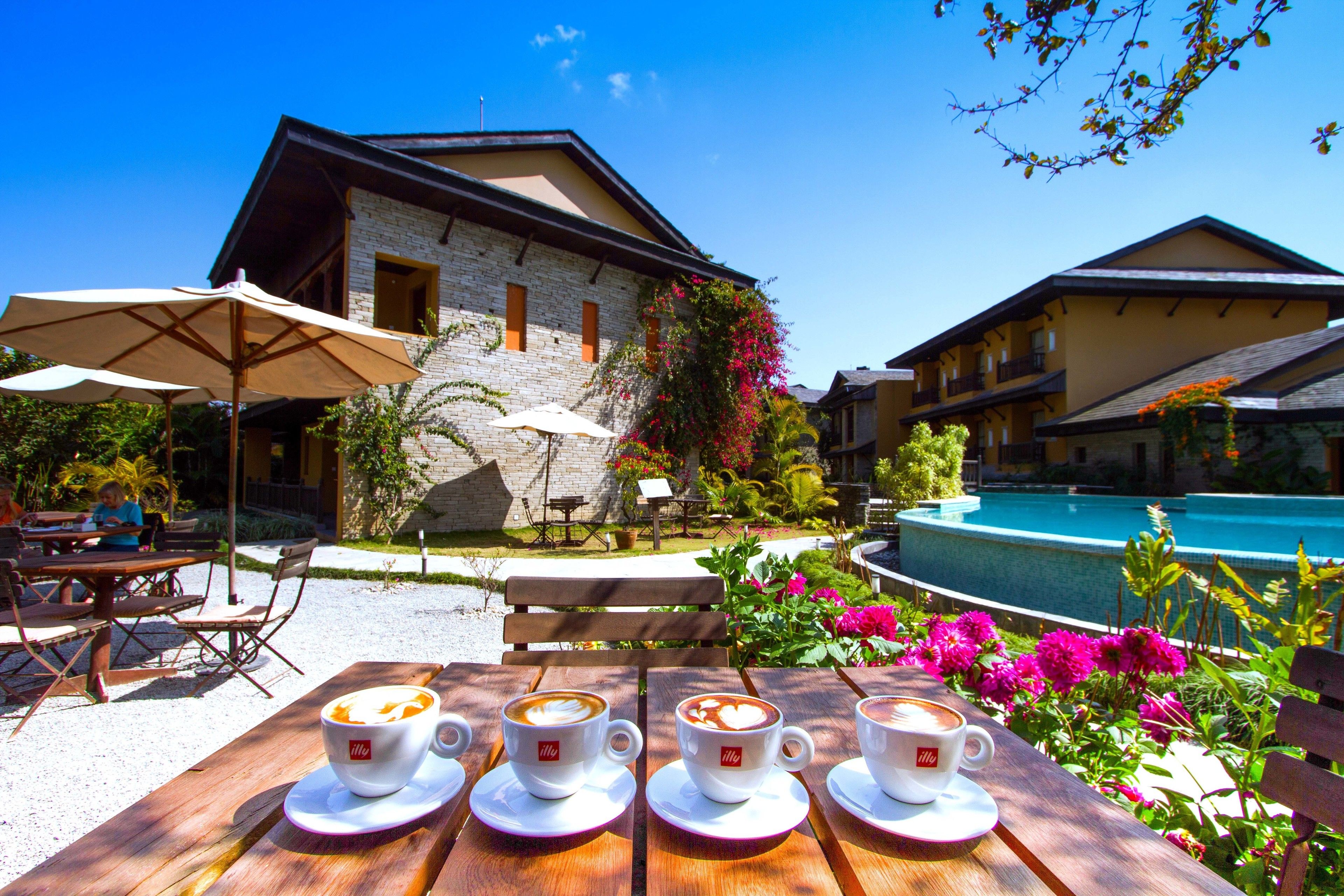 Una mesa de madera con cuatro tazas de café, una piscina y un edificio de fachada de piedra.