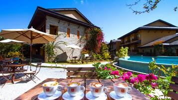 Una mesa de madera con cuatro tazas de café, una piscina y un edificio de fachada de piedra.