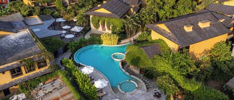 Vista aérea de un resort con una gran piscina, varias zonas de descanso y abundante vegetación.