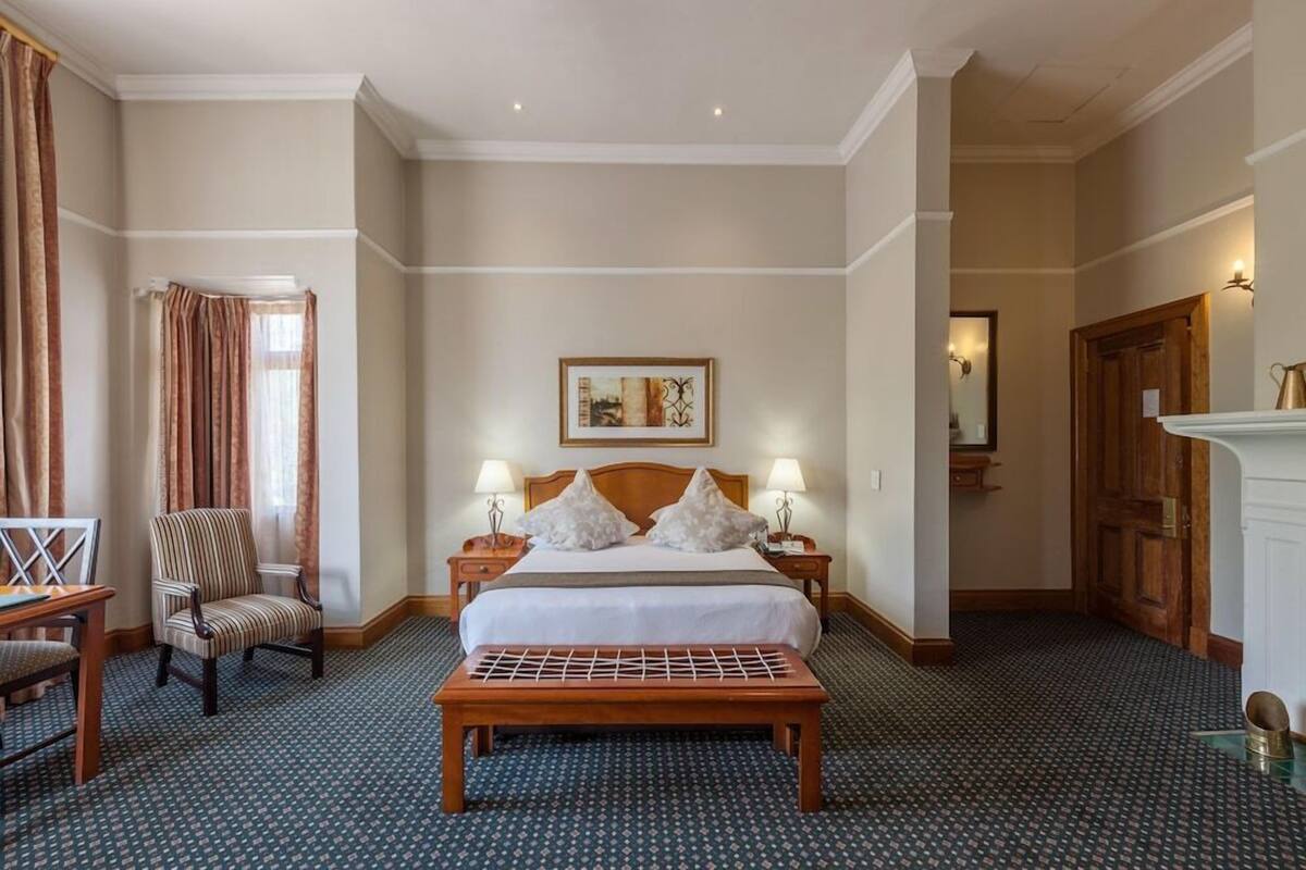 Ein Hotelzimmer mit einem großen Bett, zwei Nachttischen mit Lampen, einem Sessel, einer Bank und einem Bild an der Wand.