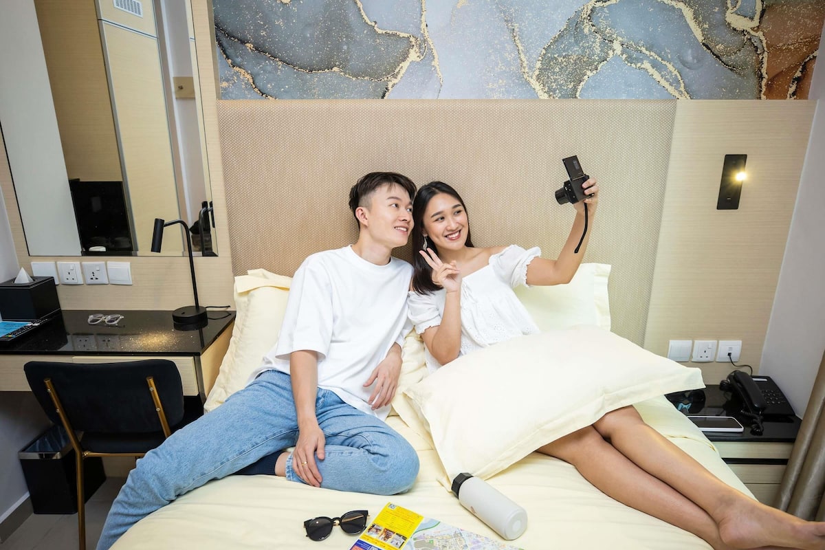 A hotel room with a bed, a desk, a chair, a mirror, and a wall with a textured design.
