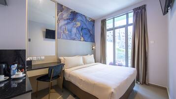 Quarto de hotel com cama, escrivaninha, cadeira, espelho grande e janela com cortinas.